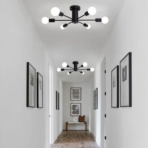 Modern black ceiling light fixture in a hallway with white walls and framed pictures.