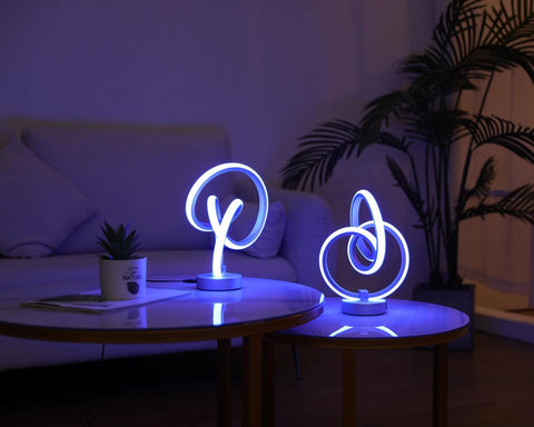 Neon light fixtures on a table in a dimly lit room with a plant and sofa in the background.