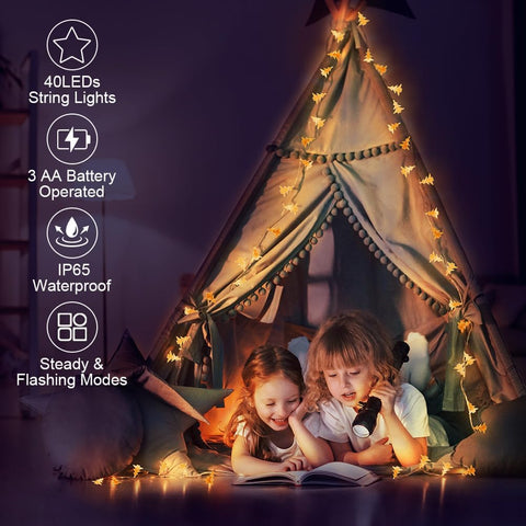 Children reading under a tent with string lights in a dark room