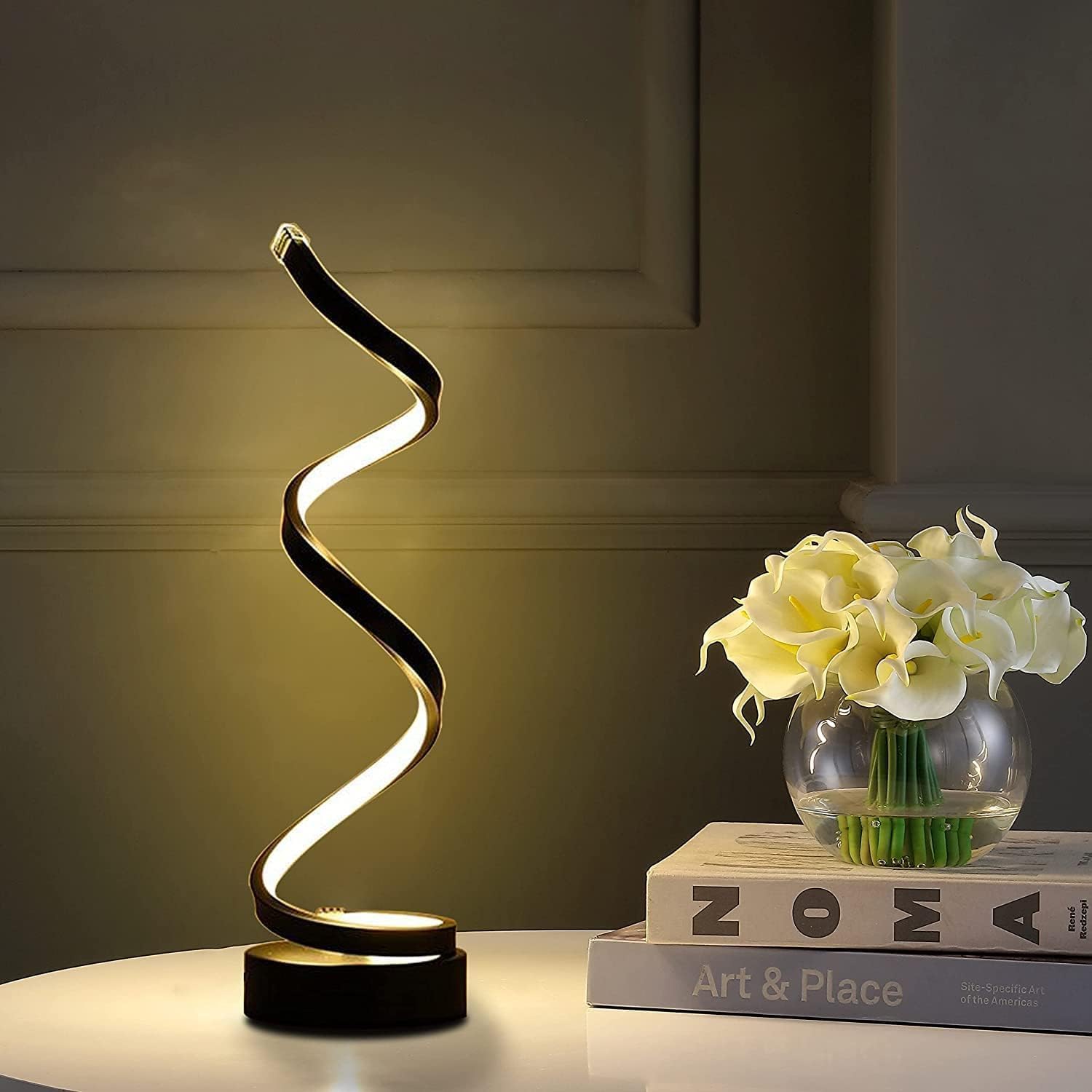 Modern table lamp with a wavy design on a surface with books and flowers.
