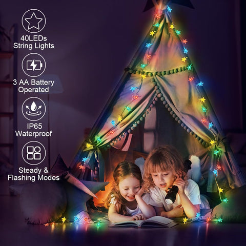 Children reading under a teepee with colorful string lights inside a dark room.