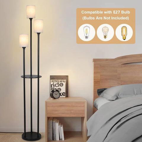 Black floor lamp with two shelves in a bedroom setting, next to a wooden nightstand with books and a clock.