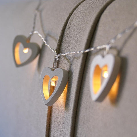 String of wooden heart lights draped over a wedding arch.

