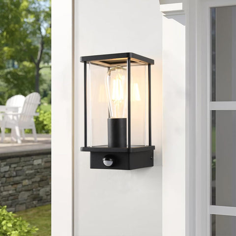 Black outdoor wall light fixture on a white wall with a garden view in the background.