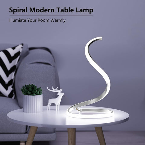 Spiral modern table lamp on a small round table with decorative items, against a gray wall.