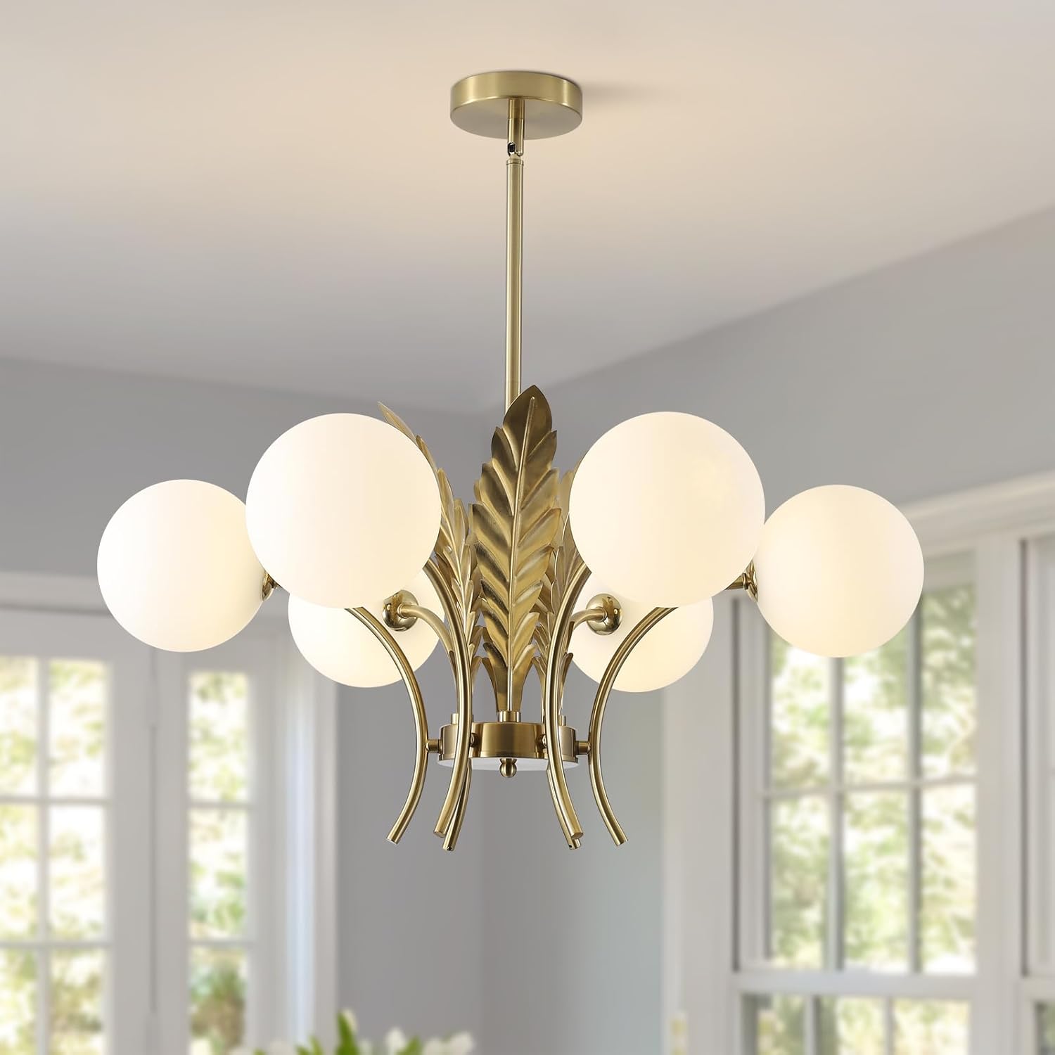 Modern chandelier with gold finish and white glass shades in a room with large windows.