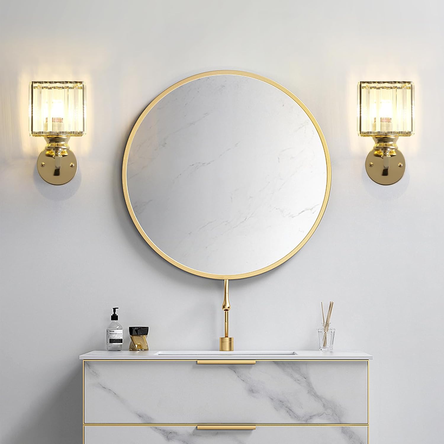 Round mirror with gold frame above a marble vanity with two wall lights.