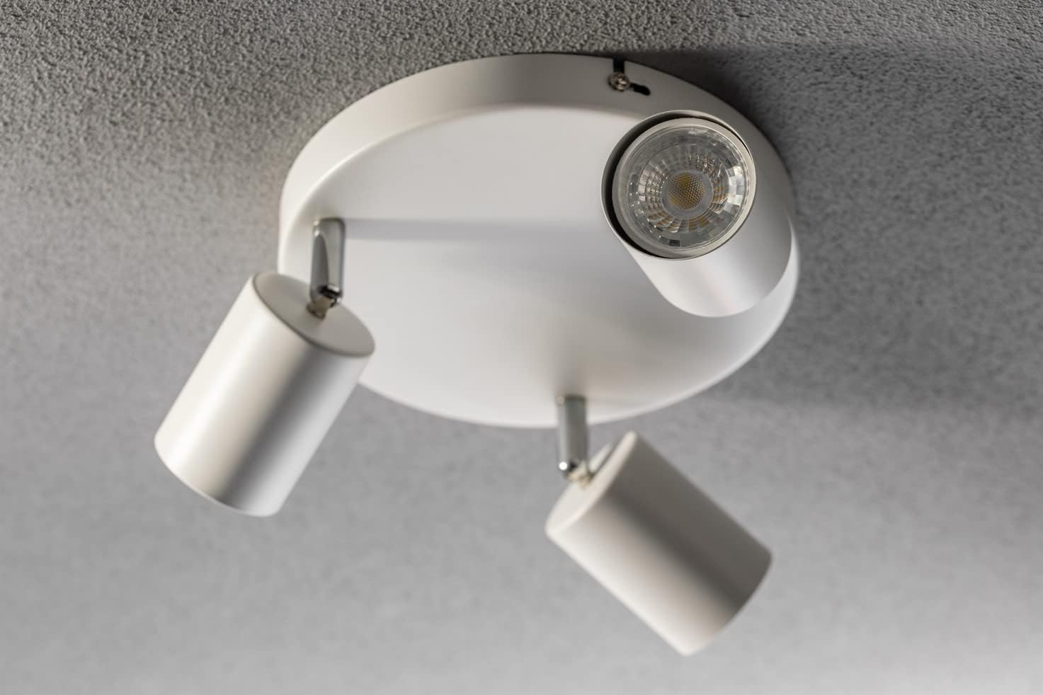 Ceiling light fixture with three white cylindrical lamps on a gray ceiling.