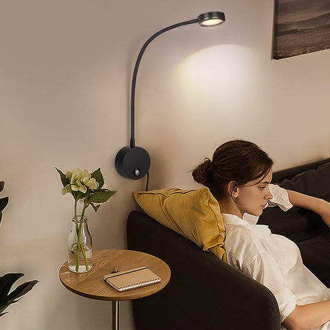 Woman sitting on a couch next to a wall-mounted lamp in a cozy living room.