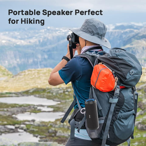 Person hiking with a backpack and portable speaker, set against a mountainous landscape.