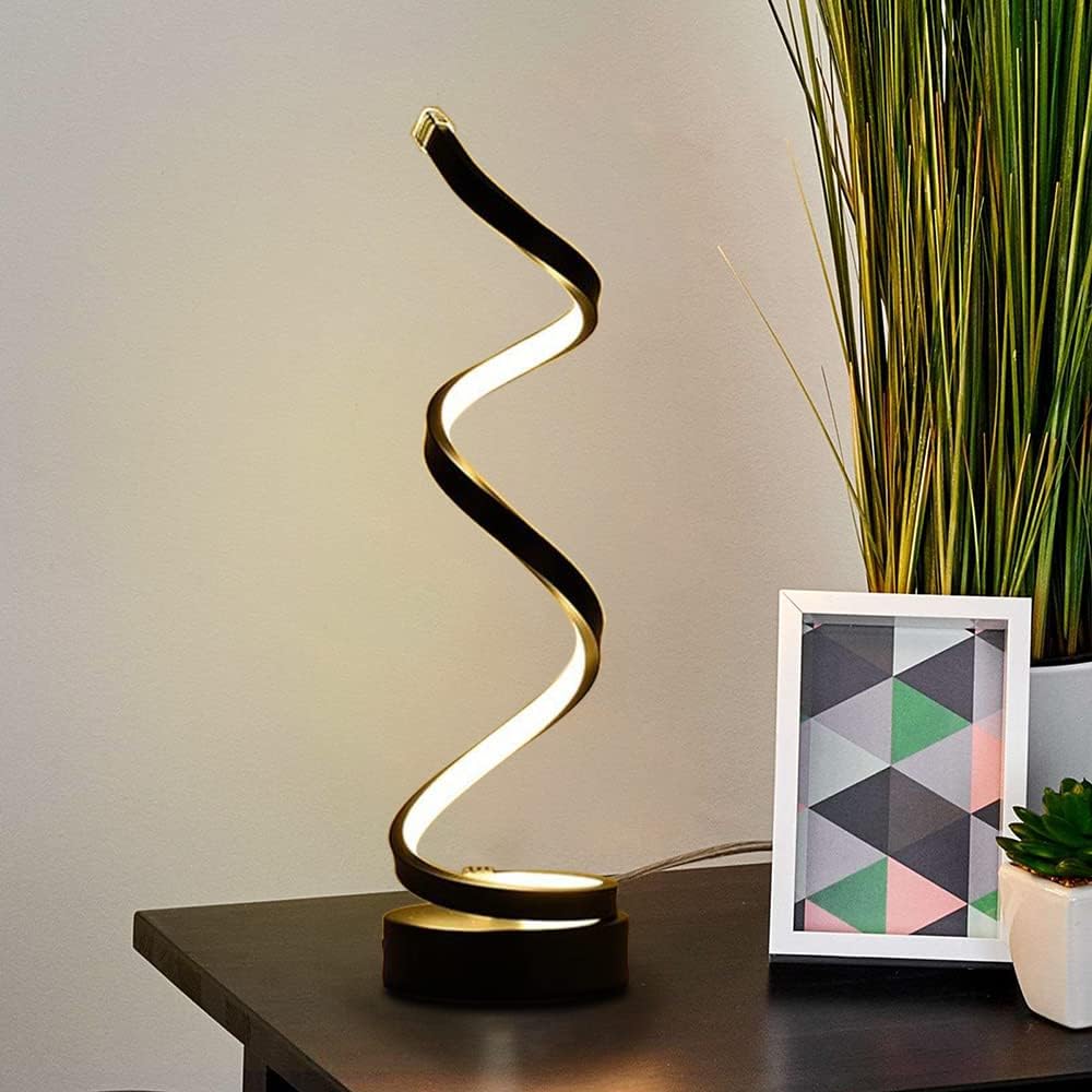 Modern table lamp with a spiral design on a desk next to a plant and framed picture.