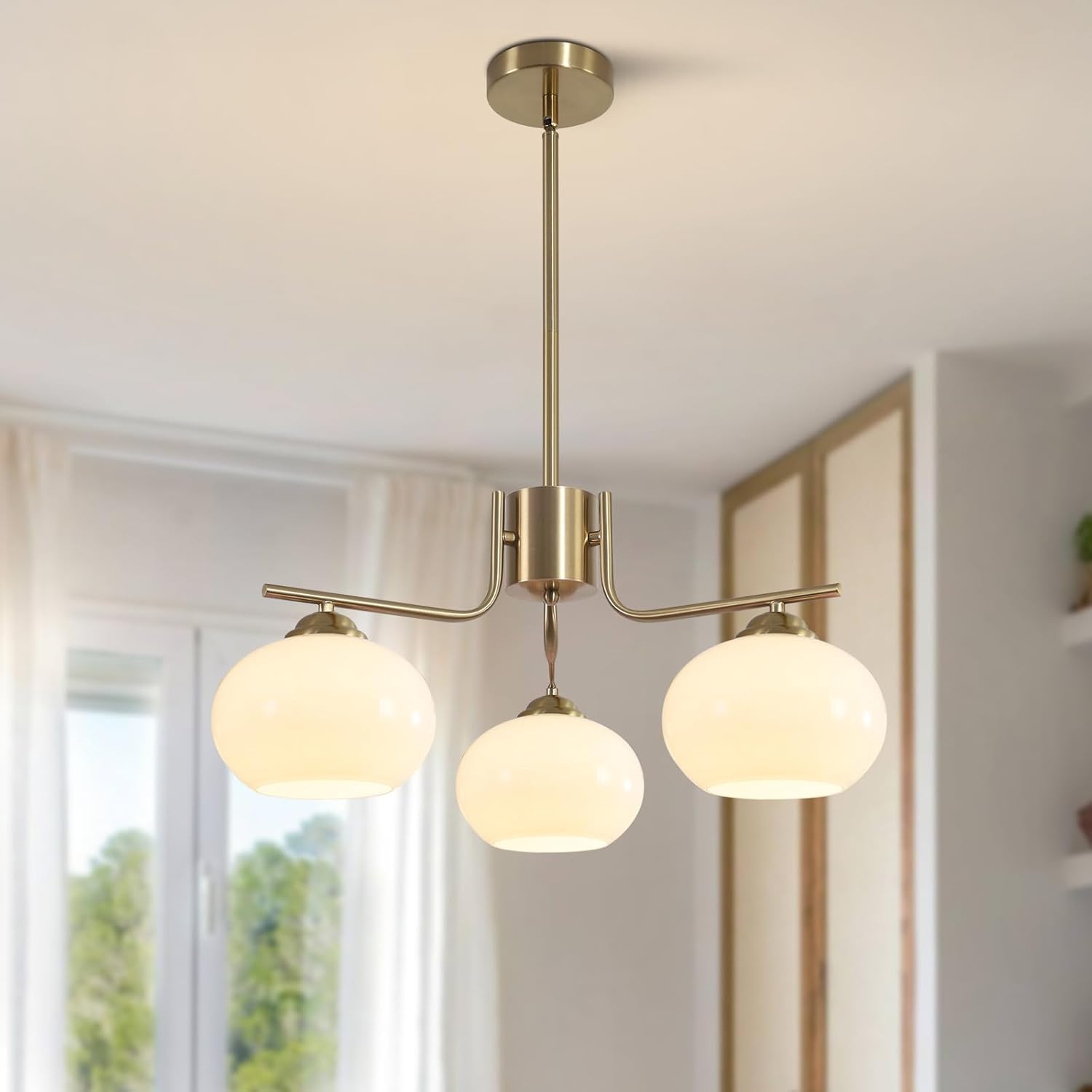 Modern pendant light fixture with three glass shades in a room with a window.
