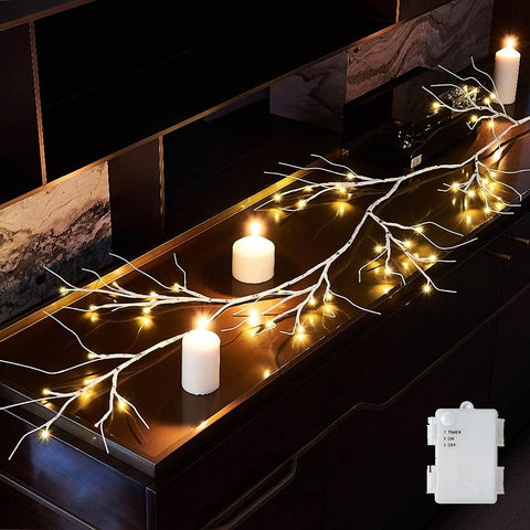 Decorative setup with lit branches and candles on a dark surface, featuring a switch for controlling the lights.