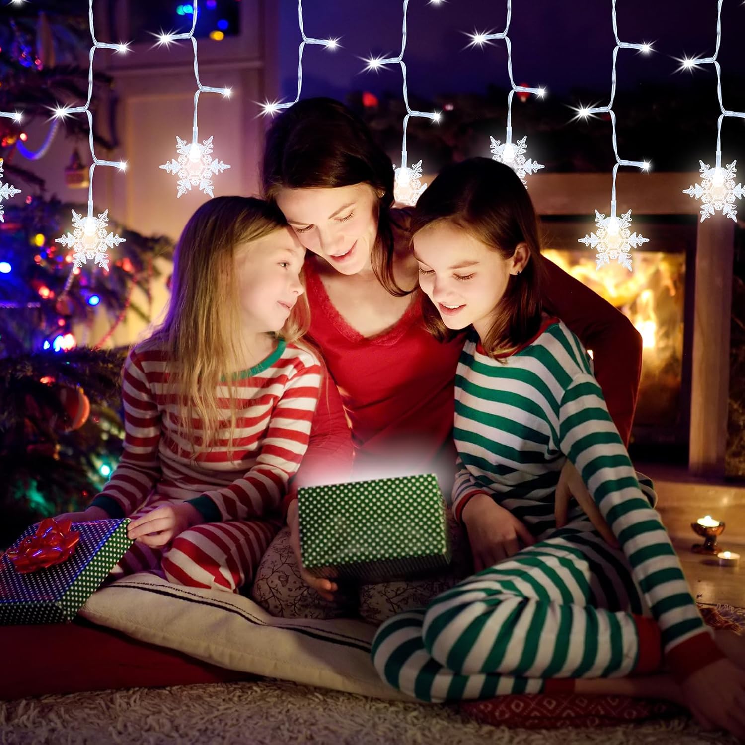 Woman and two children sitting together, looking at a glowing gift box with Christmas lights and decorations in the background.