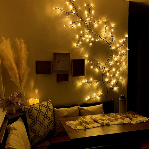 Decorative string lights on a branch in a cozy room with a table and pillows.