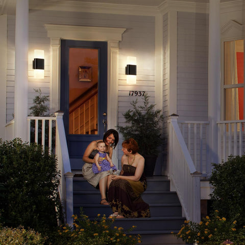Two women and a child sitting on a porch steps of a house at night.