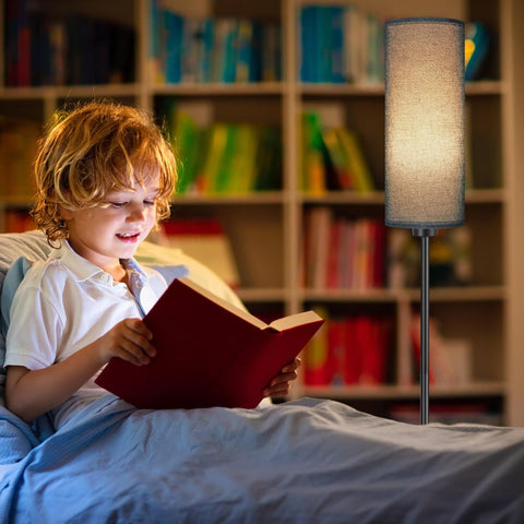 Child reading a book in bed with a lamp providing light