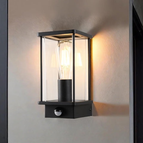 Black outdoor wall light fixture with clear glass cover on a wall.