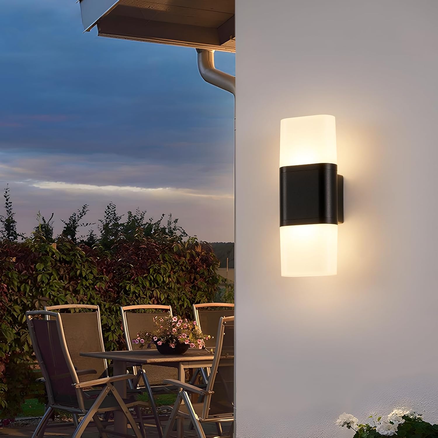 Outdoor wall light fixture on a house exterior with a patio table and chairs in the background.