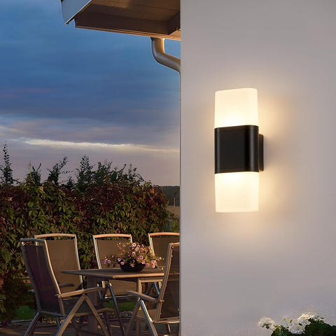 Outdoor wall light fixture on a house exterior with a patio table and chairs in the background.