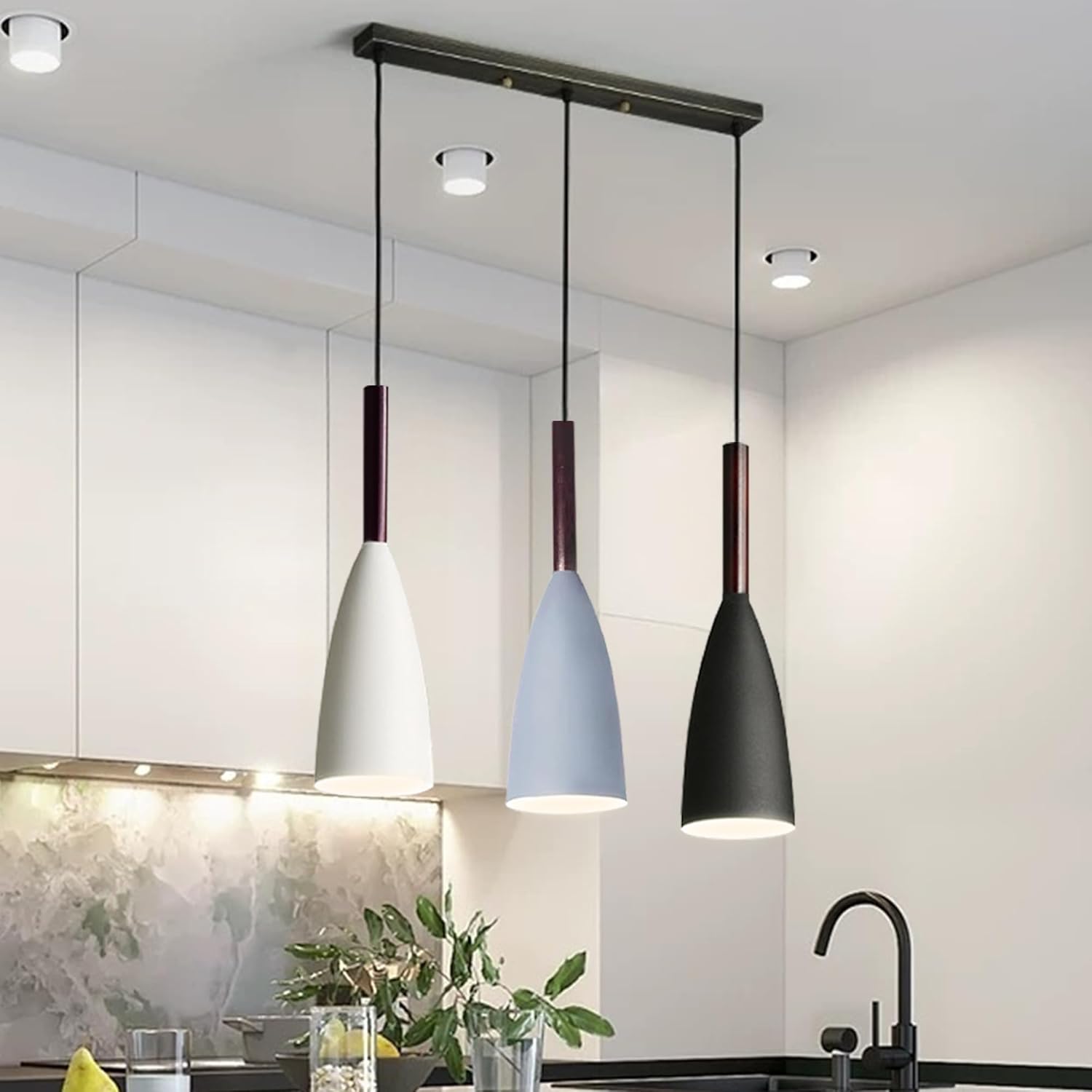 Three pendant lights in white, blue, and black hanging above a kitchen counter.