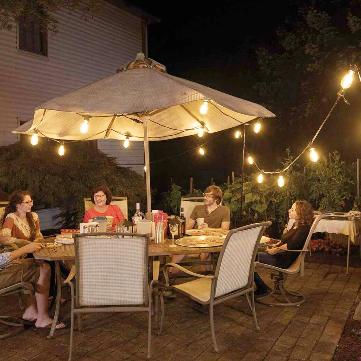People sitting at an outdoor dining table under a large umbrella with string lights.