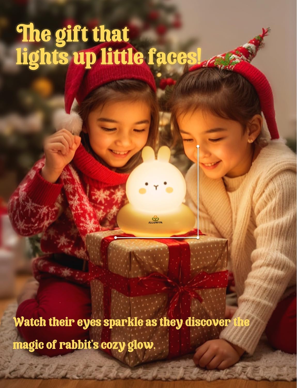 Two children wearing Santa hats with a rabbit-shaped night light on a gift, Christmas tree in the background.