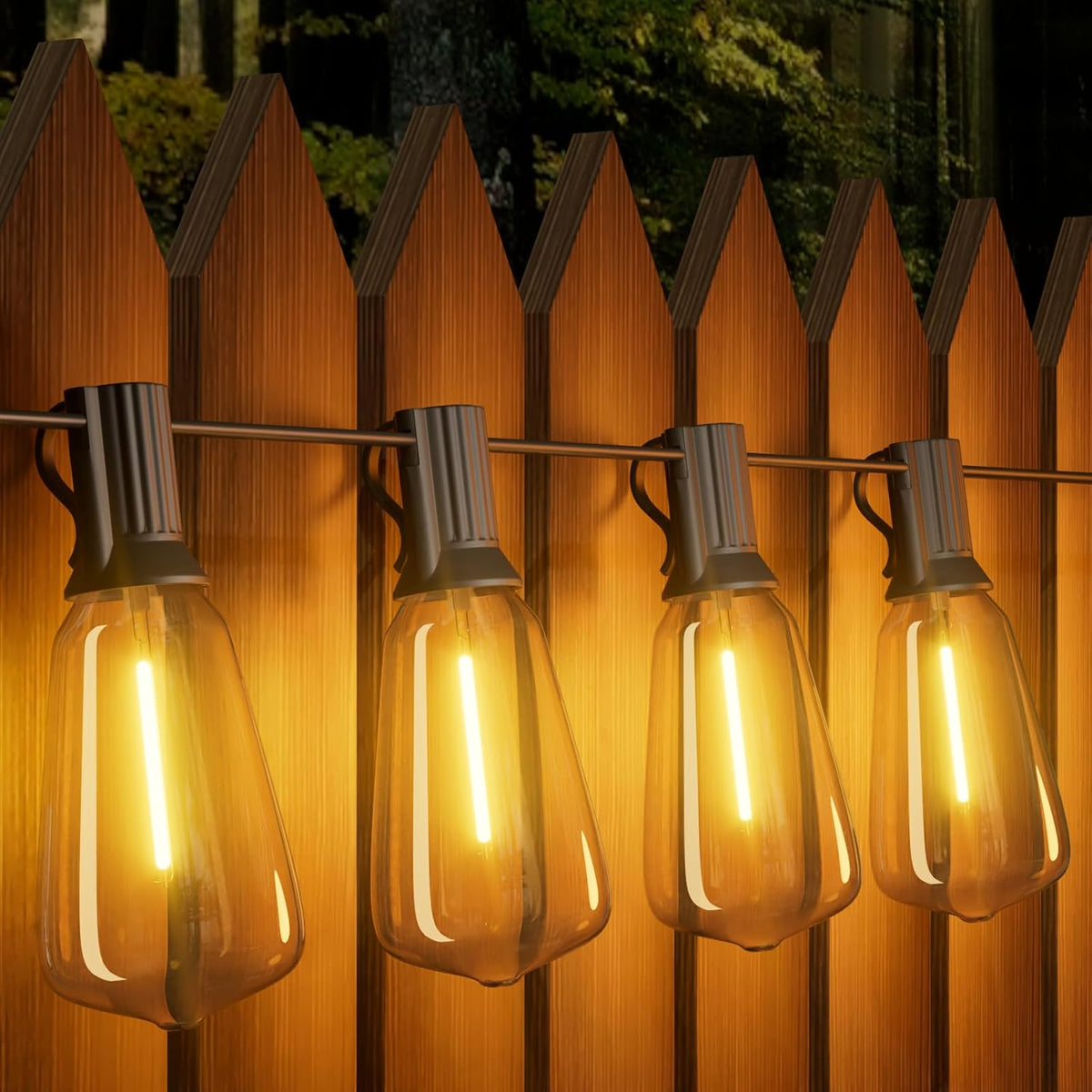 String of illuminated light bulbs hanging against a wooden fence at night.