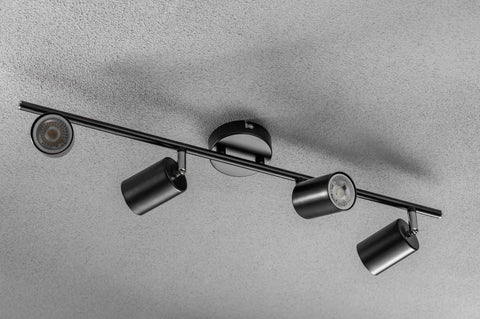 Black ceiling light fixture with four cylindrical lights on a gray background