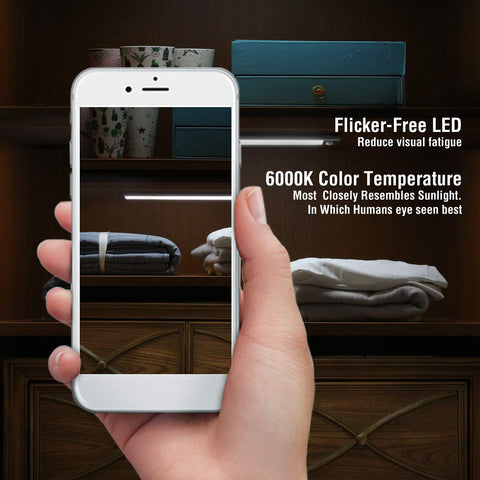 Hand holding a smartphone displaying a room with a dresser, with text about flicker-free LED and color temperature.