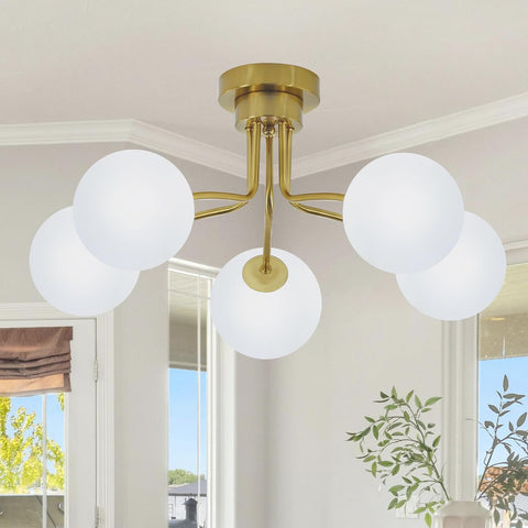 Ceiling light fixture with gold finish and white glass globes in a room with windows and plants.