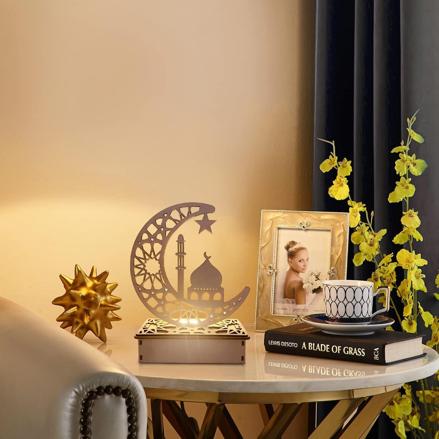 Decorative setup with a lamp, photo frame, books, and flowers on a table.