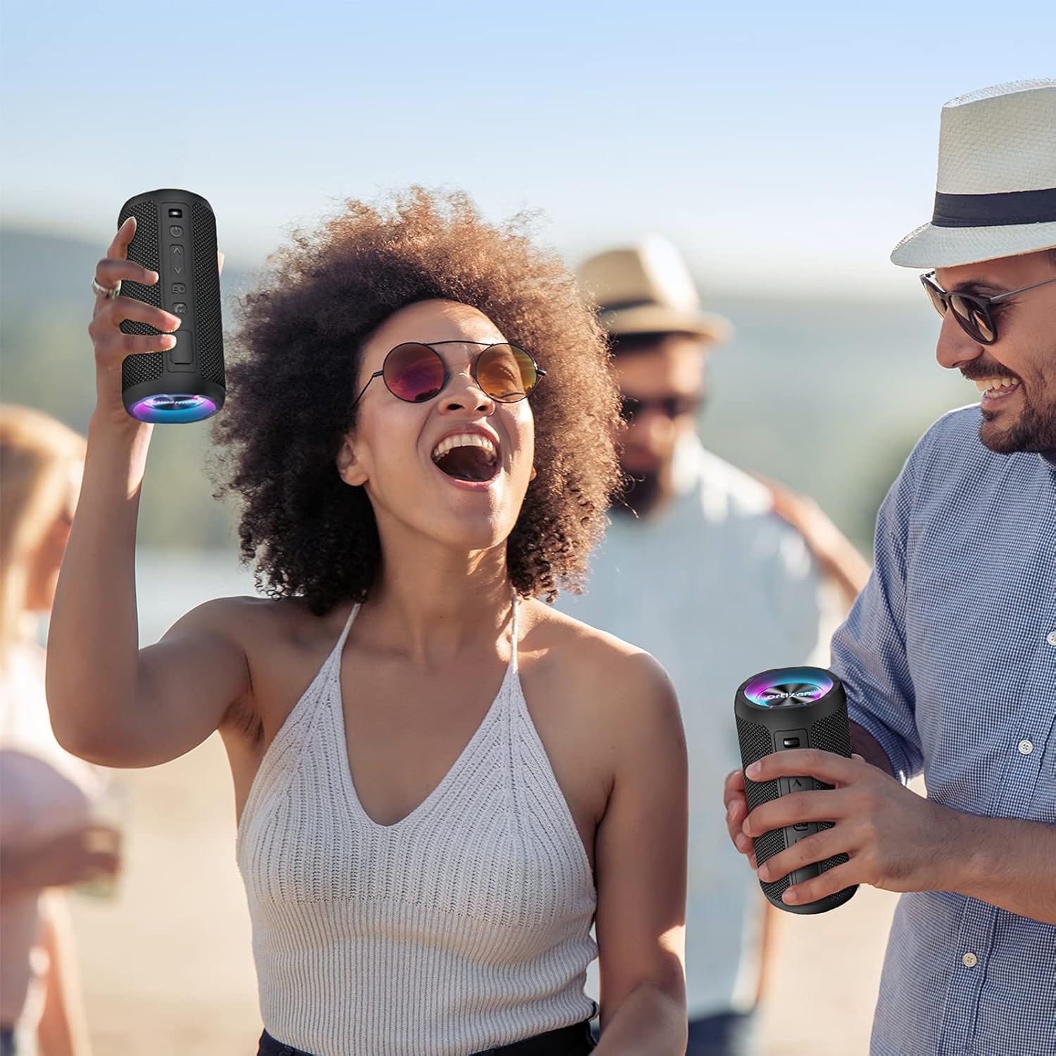 Two people holding portable speakers outdoors with a clear sky background