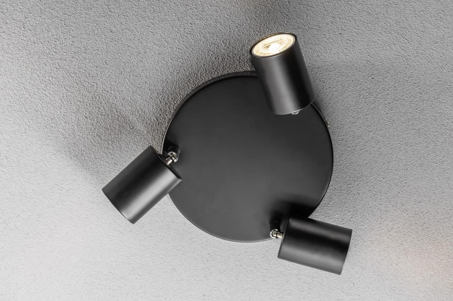 Black ceiling light fixture with three adjustable arms on a gray ceiling.