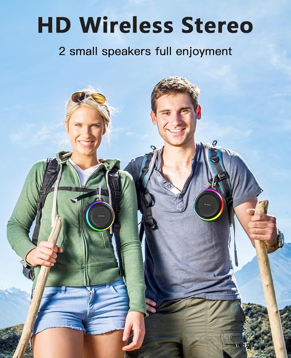 Two people hiking with wireless stereo speakers on backpacks against a mountainous background.