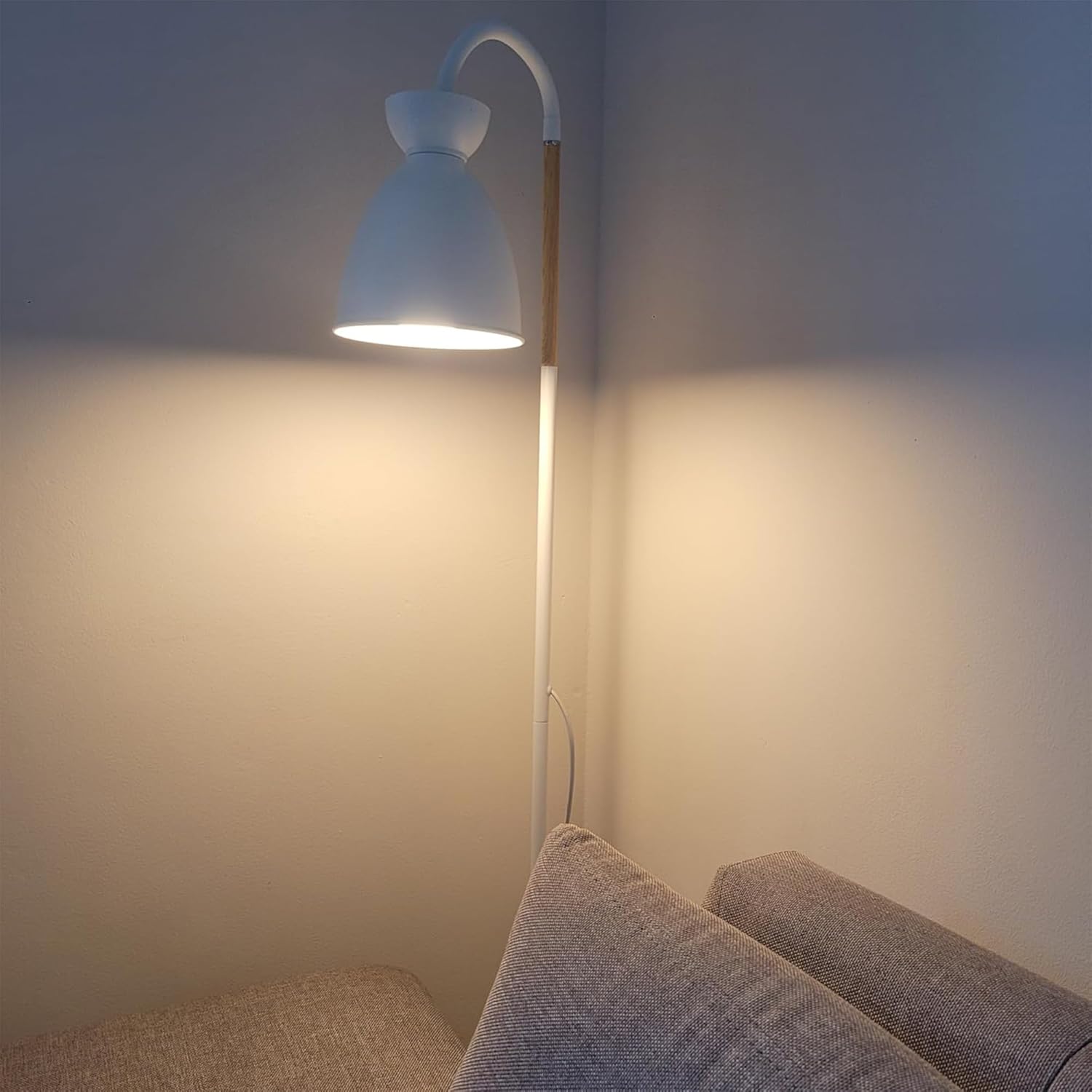 White floor lamp with a curved neck next to a sofa in a dimly lit room.