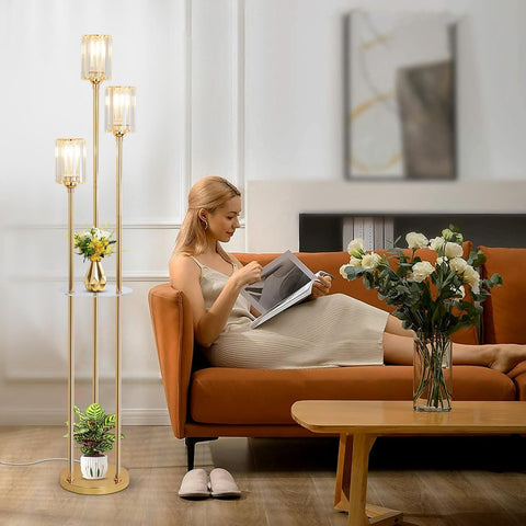 Woman reading a magazine on an orange couch in a modern living room with decorative floor lamps and plants.