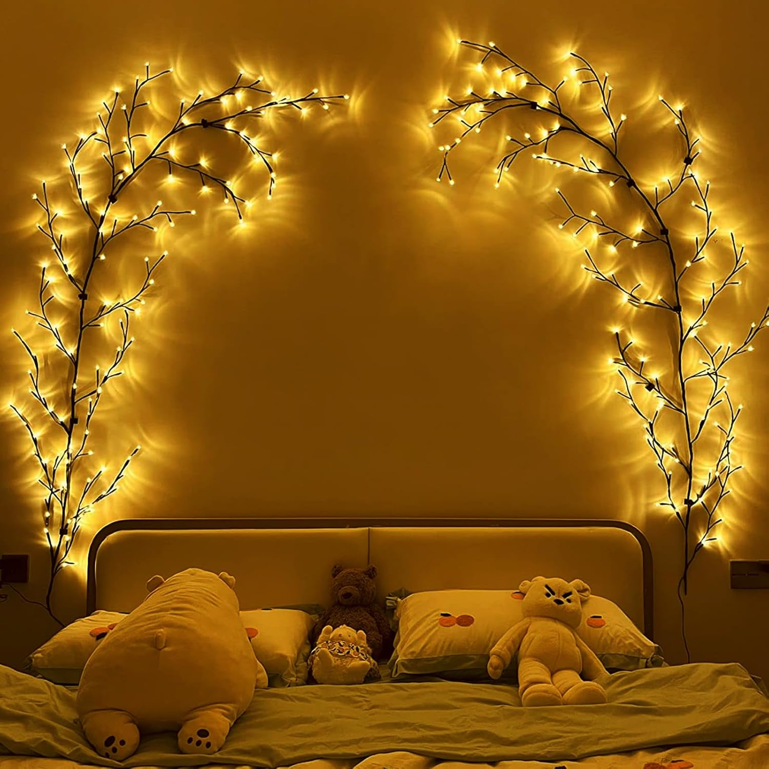 Decorative string lights shaped like branches above a bed with teddy bears and pillows.