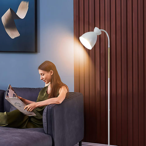 Woman reading a magazine on a couch next to a floor lamp with a curtain in the background