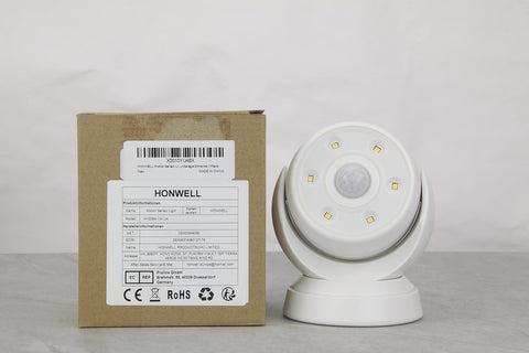White motion sensor next to its packaging box on a gray surface with a white background