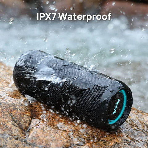 Waterproof Bluetooth speaker with IPX7 rating being tested by water on a rock.