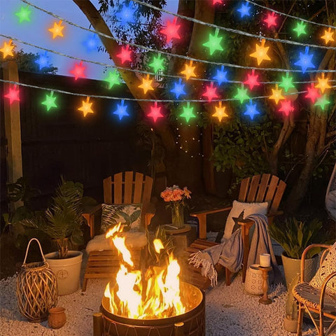 Outdoor setting with a fire pit, chairs, and colorful string lights in a garden.