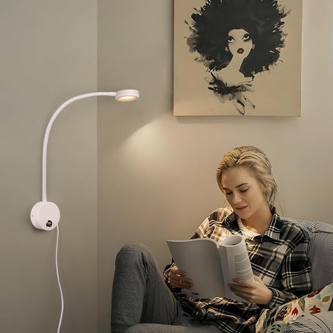 Woman reading a book in a cozy room with a wall-mounted lamp and abstract art on the wall.