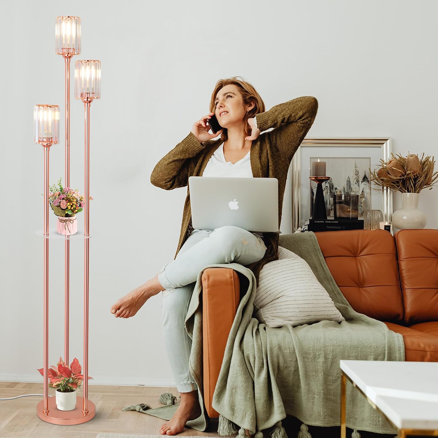 Woman sitting on a brown couch with a laptop, talking on the phone, in a room with a tall floor lamp and decor.