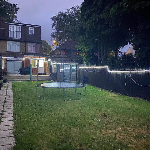 Trampoline in a backyard with a house and trees in the background
