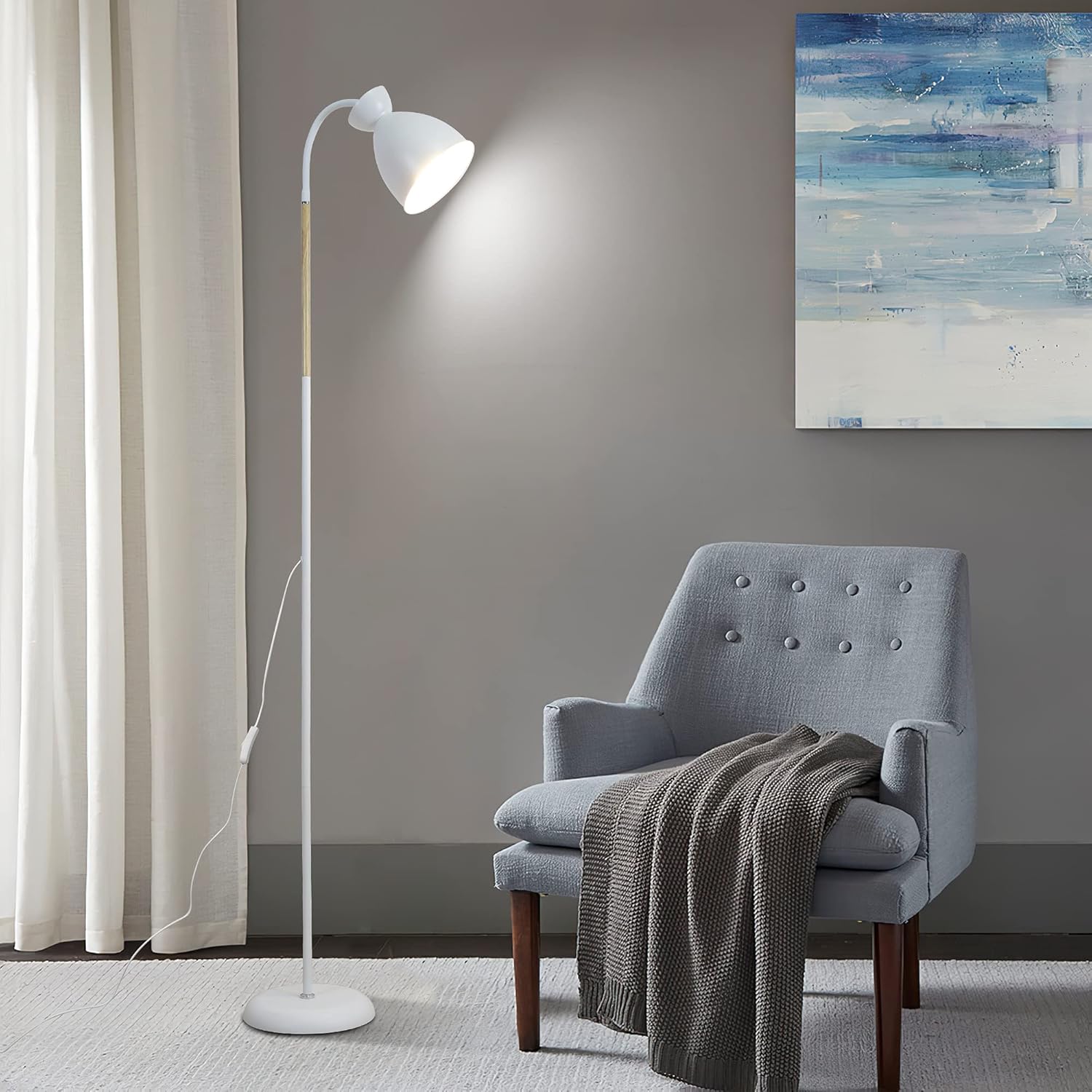 Gray armchair with a blanket next to a white floor lamp in a room with a painting on the wall.