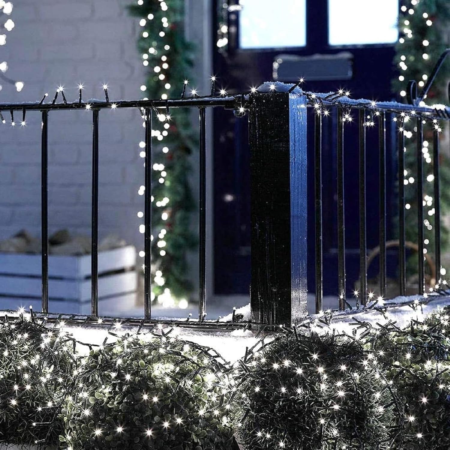 Decorative string lights on a railing and plants with a building in the background