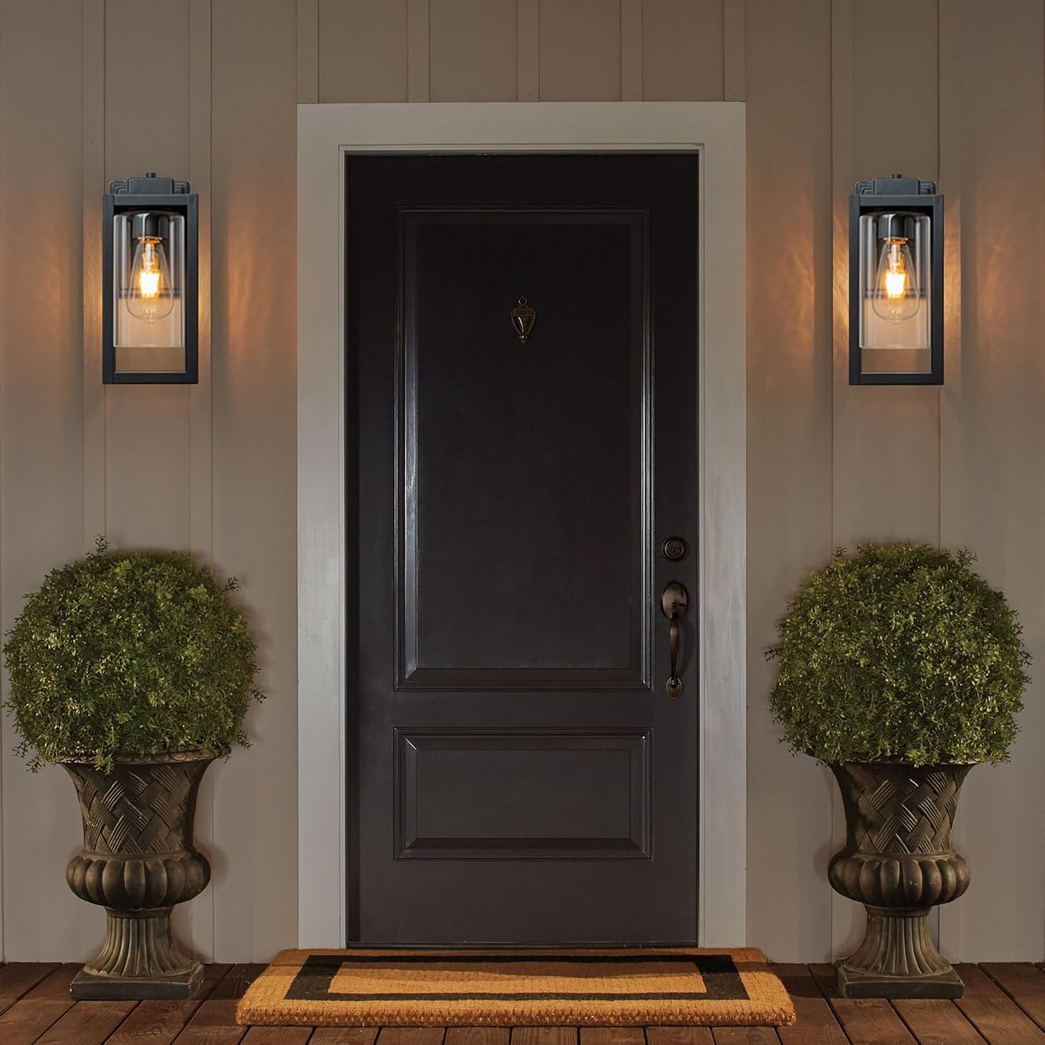 Dark wooden door with wall lights and decorative plants on a wooden deck.