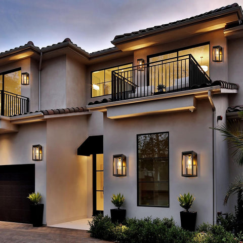Modern house exterior with balconies, lights, and plants at dusk.