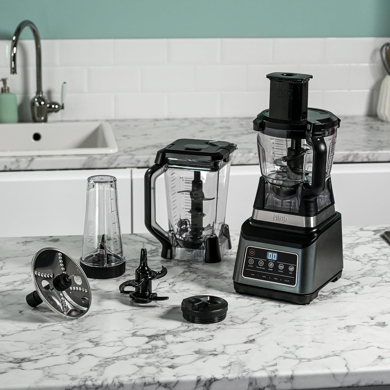 Black food processor with attachments on a marble countertop in a kitchen.